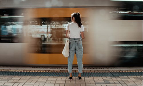 Woman standing on platform, looking at a train moving past her with a speed